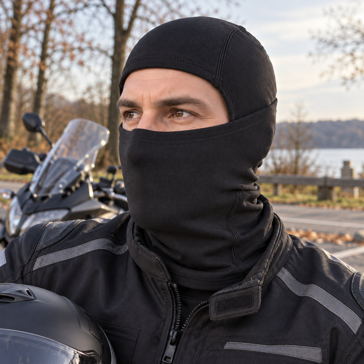 Motorradfahrer mit schwarzer PIXLII Winter Sturmhaube und Motorradhelm neben einem geparkten Motorrad